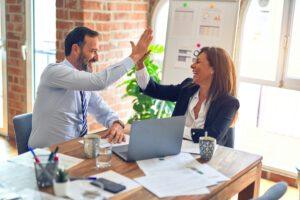 Two professionals sitting at a desk high fiving each other